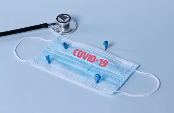Stethoscope, miniature workers and medical face mask with Covid-19 text