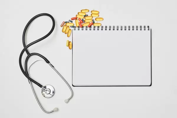 Stethoscope, pills drugs and notepad on white background