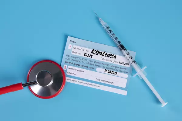 Stethoscope with AstraZeneca Covid-19 vaccination certificate and syringe on blue background