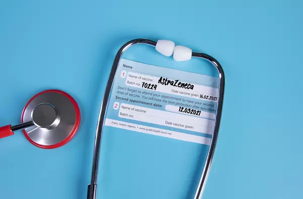 Stethoscope with AstraZeneca Covid-19 vaccination certificate on blue background