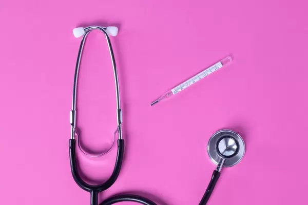 Stethoscope with thermometer on a pink background