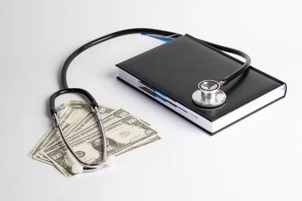 Stethoskop auf schwarzem Buch und Banknoten = Gesundheitskosten / medizinische Kosten
