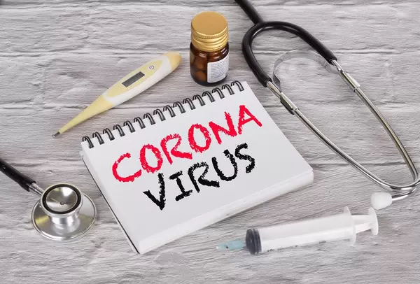 Stethoskop, Fieberthermometer, Spritze und Medizin neben einem Notizbuch mit Worten Corona Virus