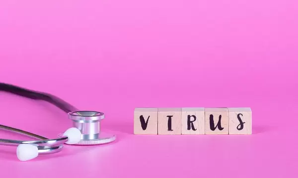 Stethoskop liegt neben Holzwürfeln mit dem Wort Virus auf pinkem Hintergrund