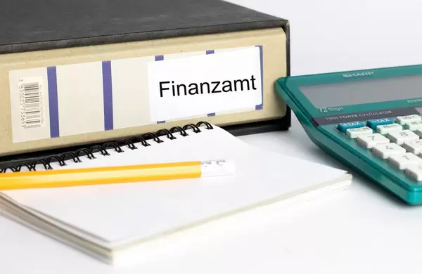 Steuererklärung - Ein Aktenordner auf den Finanzamt steht mit einer Taschenrechner, einem Notizblock und einem Bleistift