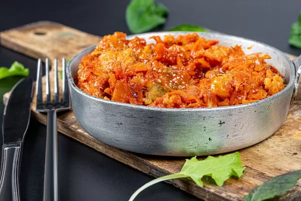 Stewed fish with tomato sauce and vegetables in a pan on the kitchen board with a knife and fork (Flip 2020)