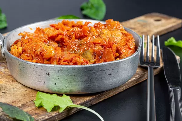 Stewed fish with tomato sauce and vegetables in a pan on the kitchen board with a knife and fork