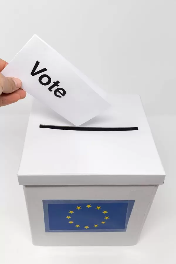 Stimmzettel in einer Hand, ruft mit der Aufschrift "Vote" zum Wählen gehen auf, während der Wahlschein in die Abstimmungsurne gesteckt wird