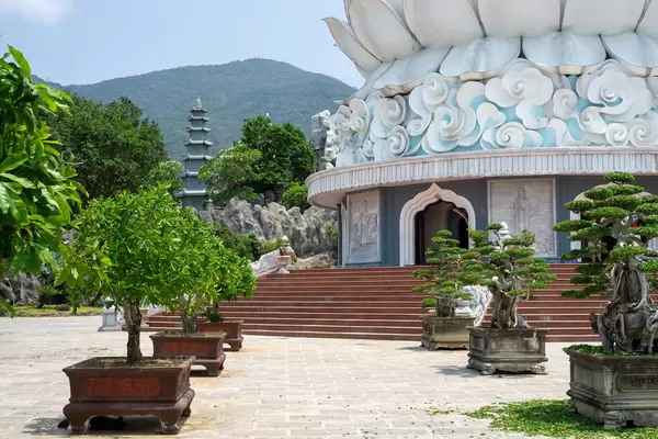 Stone Flower Pots with Small Bonsai Trees in front of the Lady Buddha Statue at Linh Ung Pagoda with Mountains in the Background in Da Nang, Vietnam