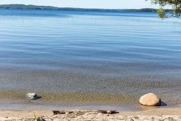 Strandabschnitt der Bucht der Insel Kelvenne in Finnland, mit Blick auf Steine im blauen See und Päijänne Nationalpark im Hintergrund