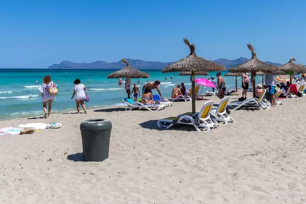 Straw parasols and plastic sun beds. Tourists on the sandy beach of Can Picafort on the island of Mallorca