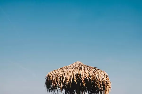 Straw umbrella on blue sky background. Summer.