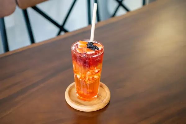 Strawberry Iced Oolong Tea with Strawberry Jelly, Sliced Strawberries and Dried Hibiscus on a Wooden Table in a Modern Cafe