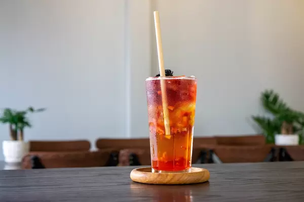 Strawberry Oolong Green Tea with Ice Cubes, Dried Hibiscus and Strawberry Cubes in a Cocktail Glass with Paper Straw on a Wooden Saucer