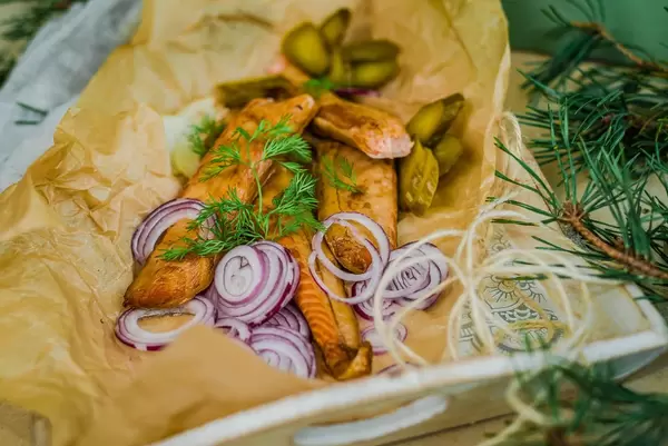 Streifen geräucherter Lachs mit Zwiebeln, Gewürzgurken und Kräutern neben Kieferzweigen