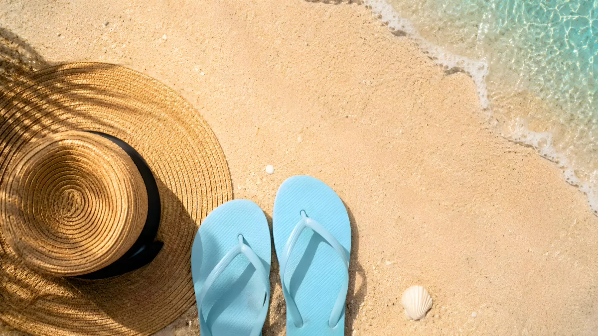 Strohhut und blaue Flip-Flops am Sandstrand