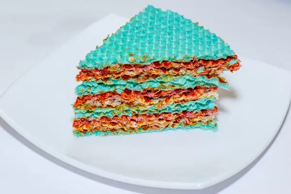 Stück eines süßen Kuchens aus bunten Waffeln und Kondensmilch vor weißem Hintergrund