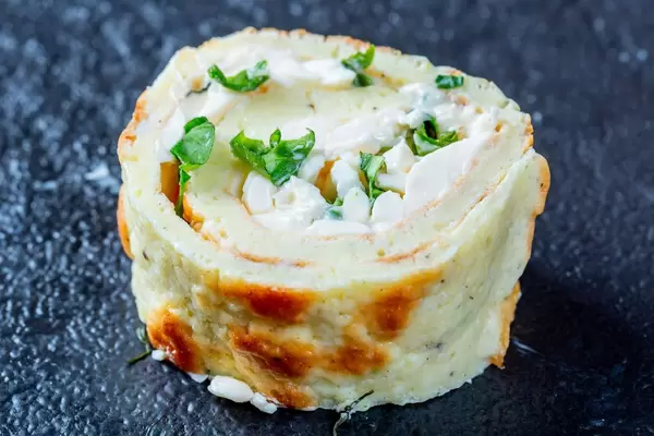 Stück gerollter Pfannkuchen gefüllt mit Hüttenkäse und Kräutern auf schwarzem Hintergrund