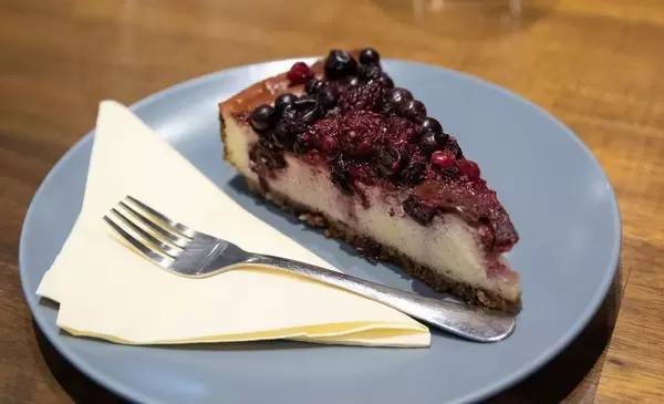 Stück hausgemachter Käsekuchen mit Beeren als Nachtisch auf blauem Teller
