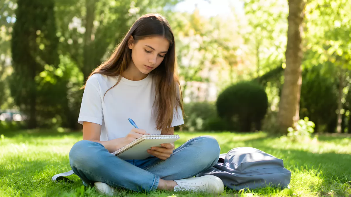 Studentin schreibt im Park auf Notizbuch im Sommer