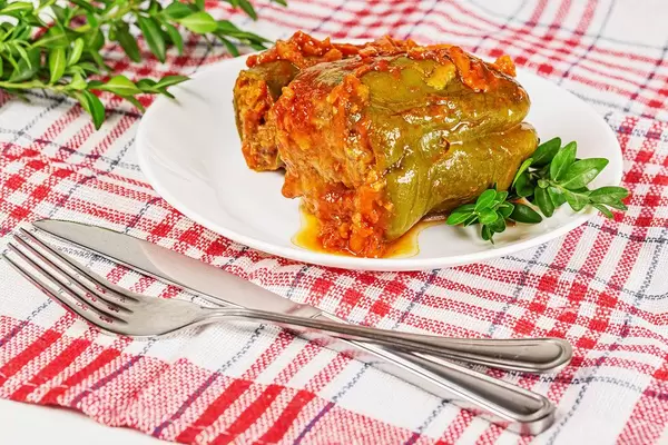 Stuffed bell peppers with tomato sauce on a kitchen towel with a knife and fork