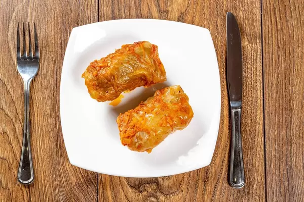 Stuffed stewed in tomato sauce with knife and fork on wooden brown background