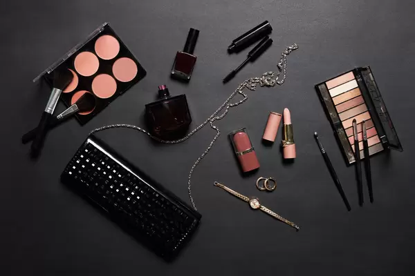 Stylish female's clutch with beauty make-up products on dark background