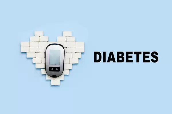 Sugar cubes and portable diabetes measuring monitor on bright blue backdrop