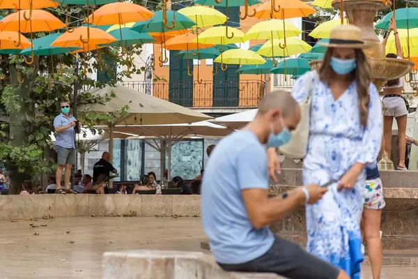 Summer 2020: tourists with face mask, smartphone or camera under the suspended umbrellas in Sóller