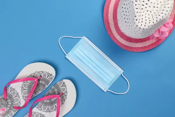 Summer beach hat with flipflops and medical face mask on blue background