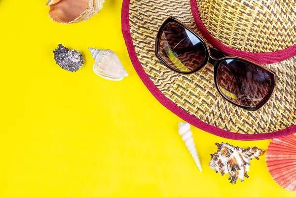 Summer vacation concept. Hat, sunglasses and shells on a yellow background with free space