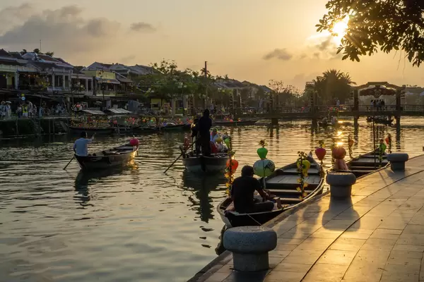 Sunset in the Ancient Town of Hoi An, Vietnam with Decorated Wooden Tourist Boats going towards the Bridge of Light at Golden Hour