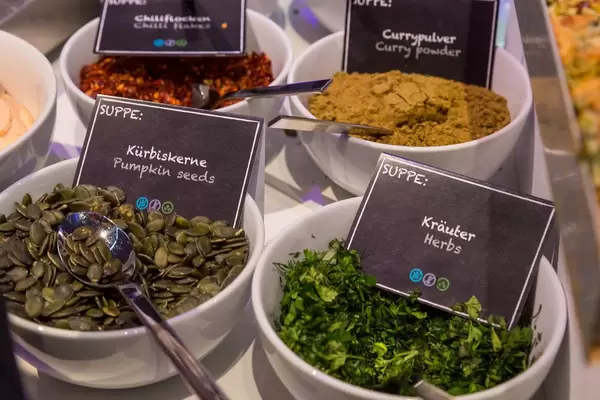 Suppentoppings in runden Behältern zum selbst schöpfen: Kürbiskerne, Kräuter, Currypulver und Chilliflocken