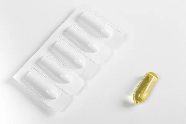 Suppositories in blister and one without packaging on white background