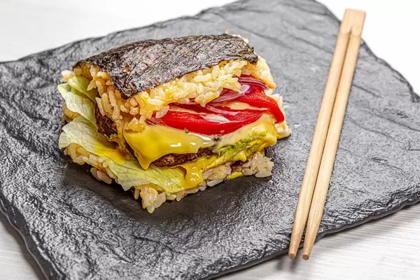 Sushi-Burger auf schwarzem Hintergrund mit Essensstäbchen