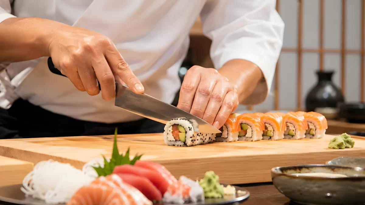 Sushi-Koch schneidet frische Maki-Rollen auf Holzbrett