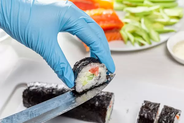 Sushi roll making preparation, close up on chef hands with a knife