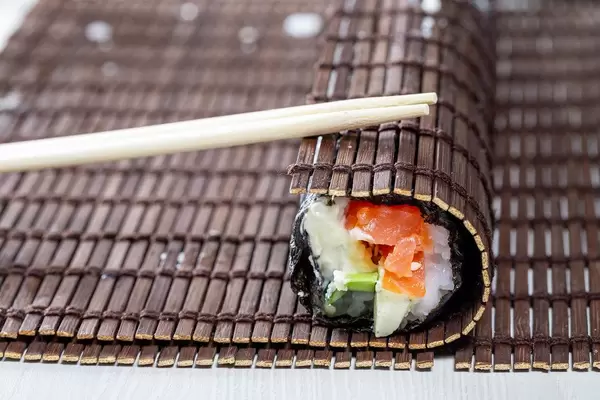 Sushi roll wrapped in bamboo Mat with chopsticks (Flip 2019)
