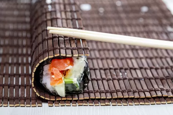 Sushi roll wrapped in bamboo Mat with chopsticks
