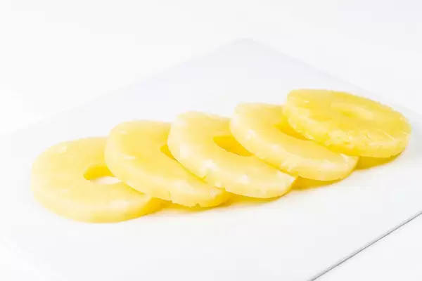 Süße Ananas Scheiben aus der Dose auf einem weißen Küchenbrett