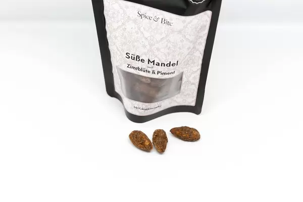 Süße Mandeln mit Zimtblüte und Piment vor weißem Hintergrund