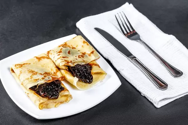 Süße Pfannkuchen mit Marmelade neben Besteck auf schwarzem Untergrund