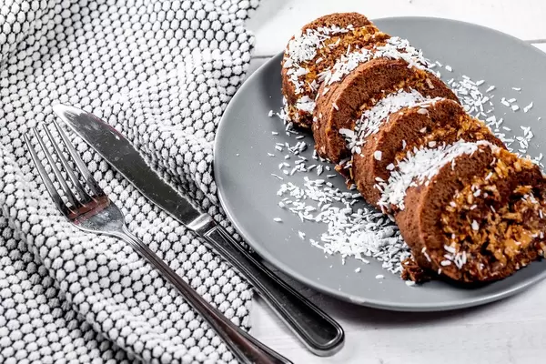 Süßer Nachtisch aus Schokoladen-Biskuit-Kuchen mit Kondensmilch, Kirschen und Kokosnussraspeln, auf einem gedeckten Tisch