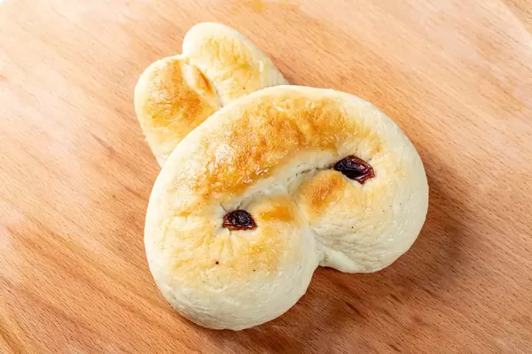 Süßes Brötchen mit Zucker und getrockneten Rosinen in Form eines Hasen auf Holztisch