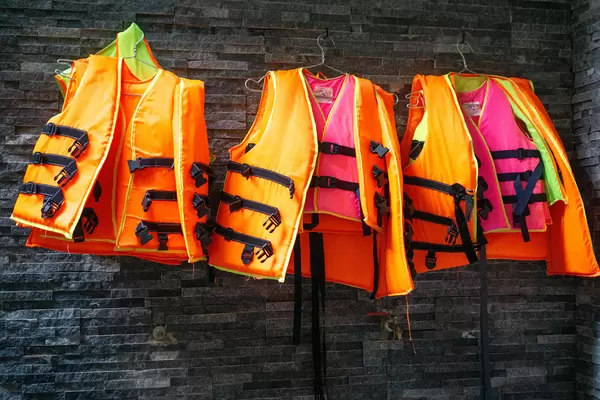 Swim Life Vests in different Colors for Adults and Children on Hangers hanging on a Wall next to a Swimming Pool in a Hotel