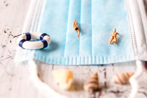 Swimming on a face mask: miniature figures on the beach protecting themselves from Covid-19 infection