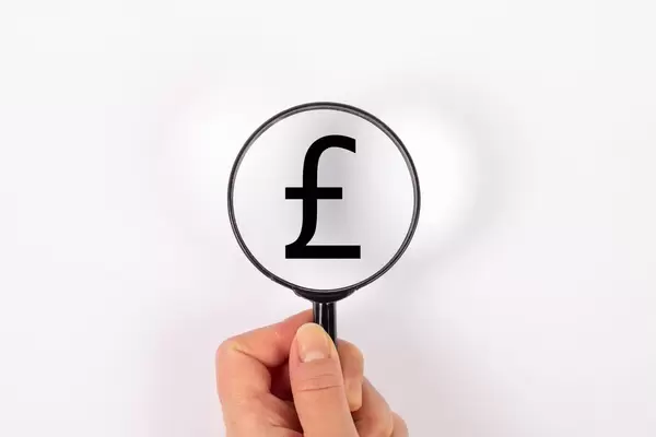 Symbol britische Pfund durch Lupe betrachtet vor weißem Hintergrund