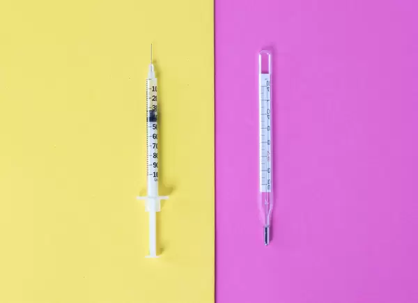 Syringe and thermometer on a yellow and pink background