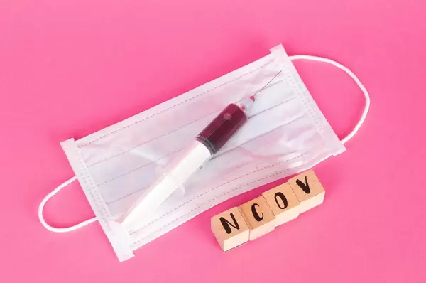 Syringe, face mask and NCOV text on pink background