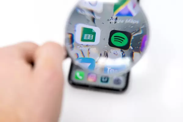 Tabellen App und Spotify App Icon auf schwarzem Smartphone durch Lupe betrachtet vor weißem Hintergrund